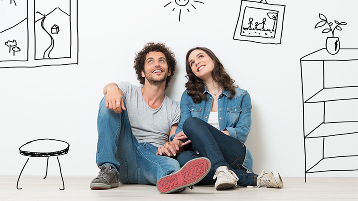 Um casal sentado no chão, com ar feliz, junto de uma parede. Estão de mãos dadas. Na parede estão desenhados  um banco. uma prateleira e alguns quadros, 